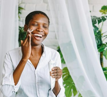 Woman Applying Face Cream and Smiling
